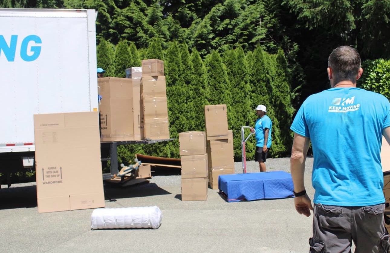 Keep Moving crew loading a moving truck with wardrobe boxes and a hand truck on a sunny day
